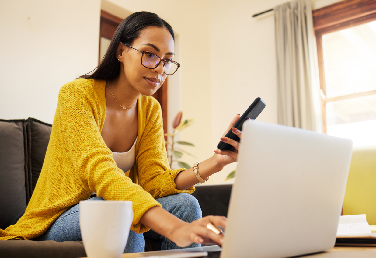 Woman sitting at home, checking her laptop and smartphone