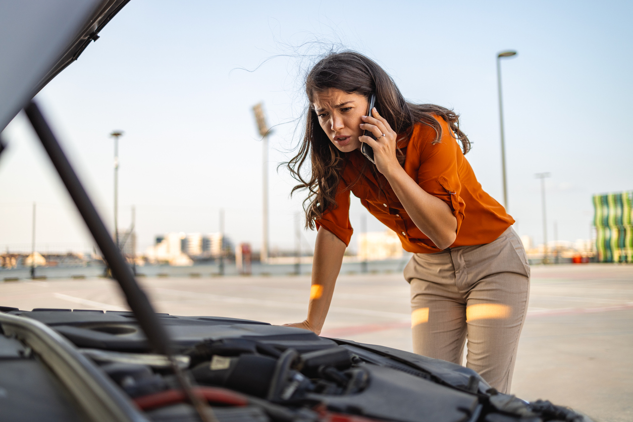 Woman on her phone next to her broken-down car with the hood popped open