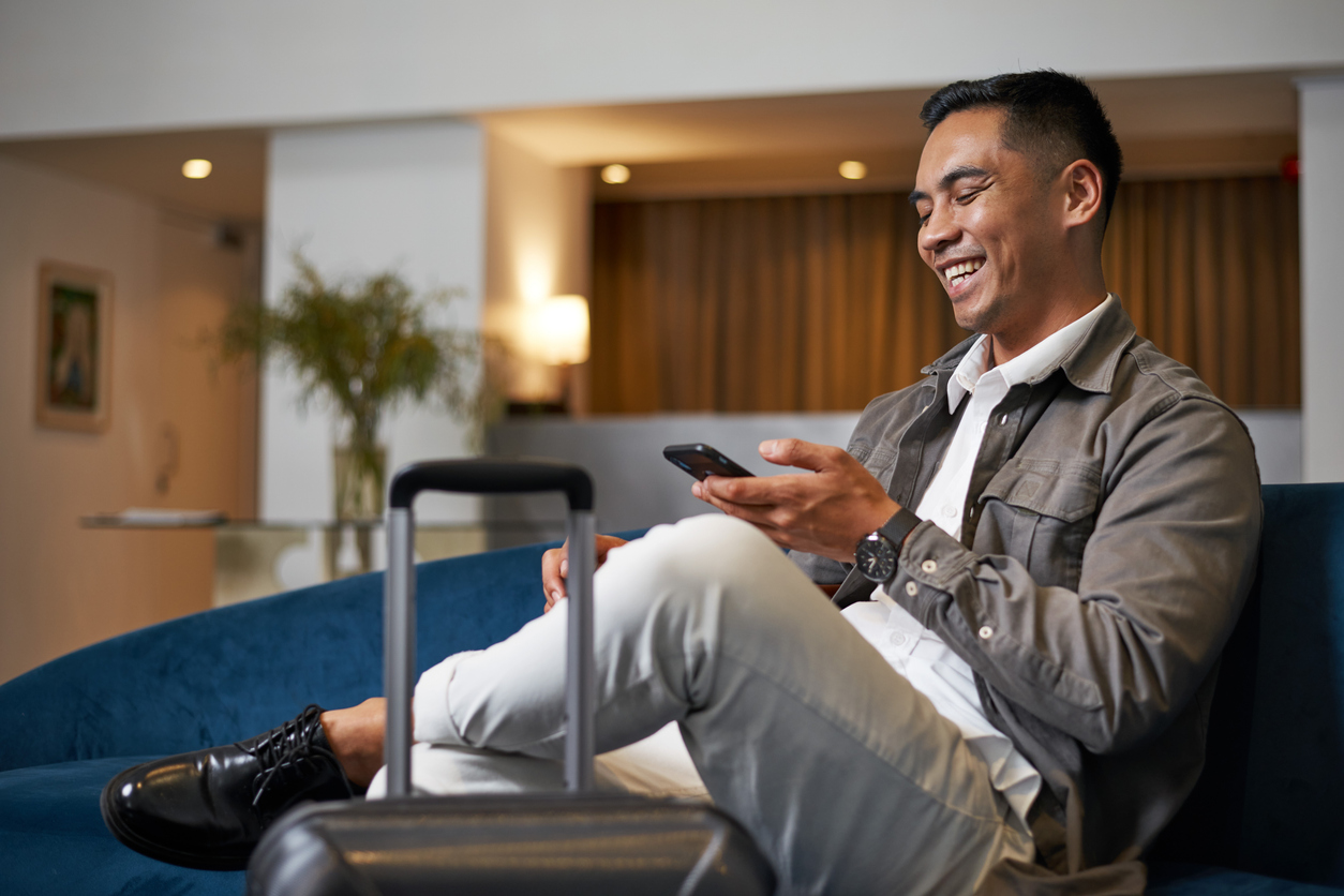 A relaxed-looking man sitting in an airport lounge, looking at his smartphone