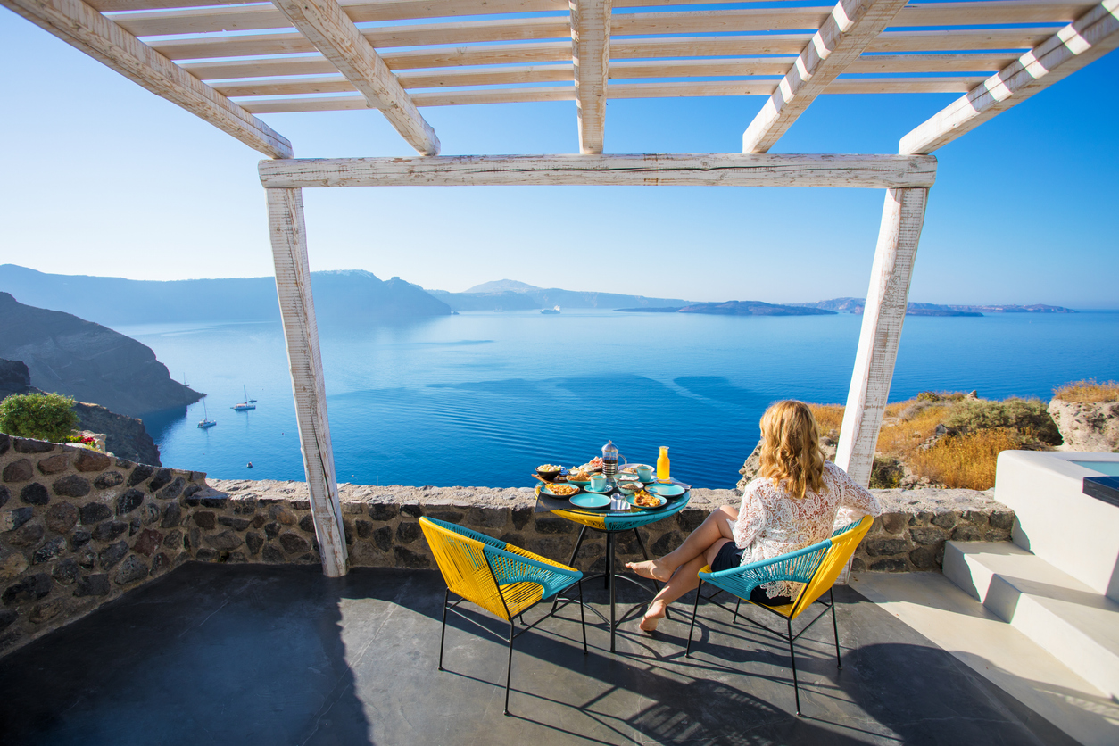 Woman enjoying breakfast on an outdoor patio with beautiful view over the sea in Santorini