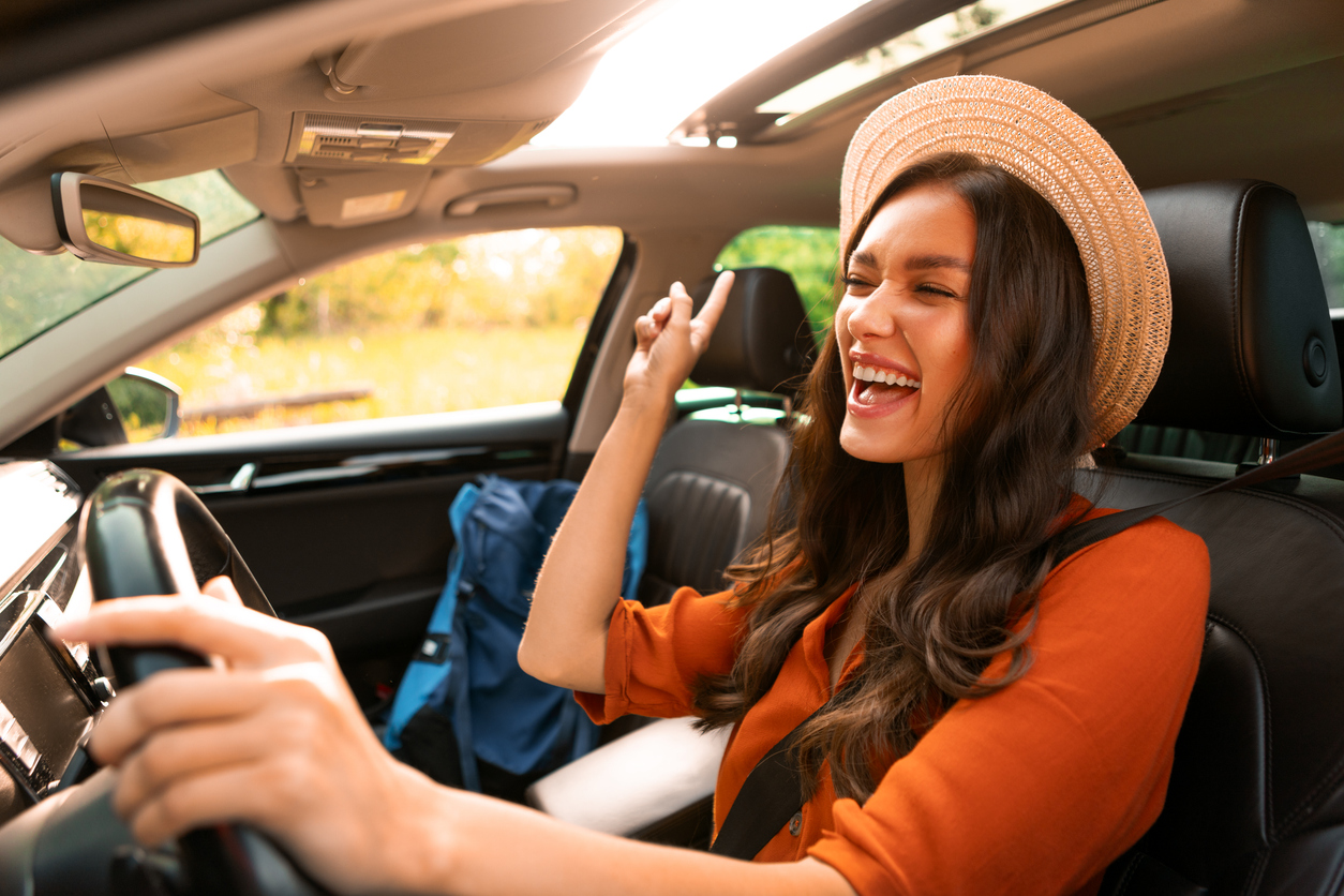 Happy woman singing while driving a car with with backpack on passenger seat