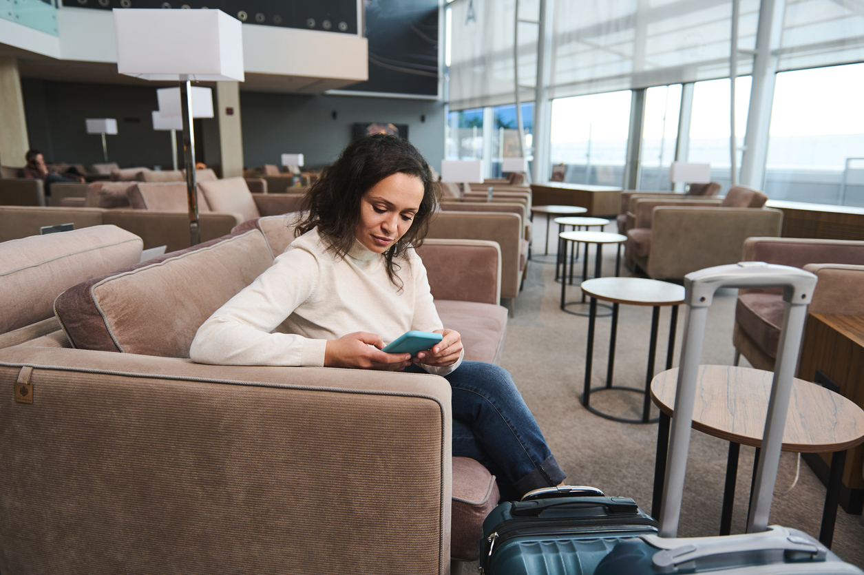Woman using mobile phone while resting on a comfortable sofa in the VIP lounge awaiting flight at airport