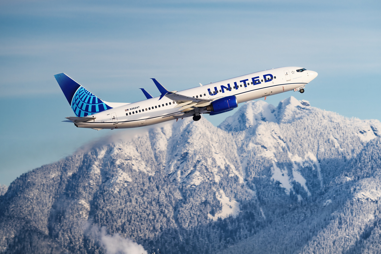 United Airlines airplane flying in the sky with mountains in the background