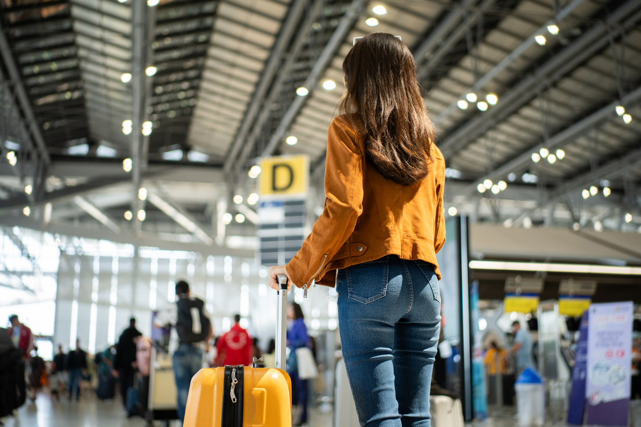 The back of a woman standing with her suitcase in a busy airport