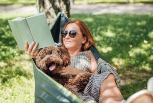 Woman relaxing in a hammock, reading a book and holding her dog