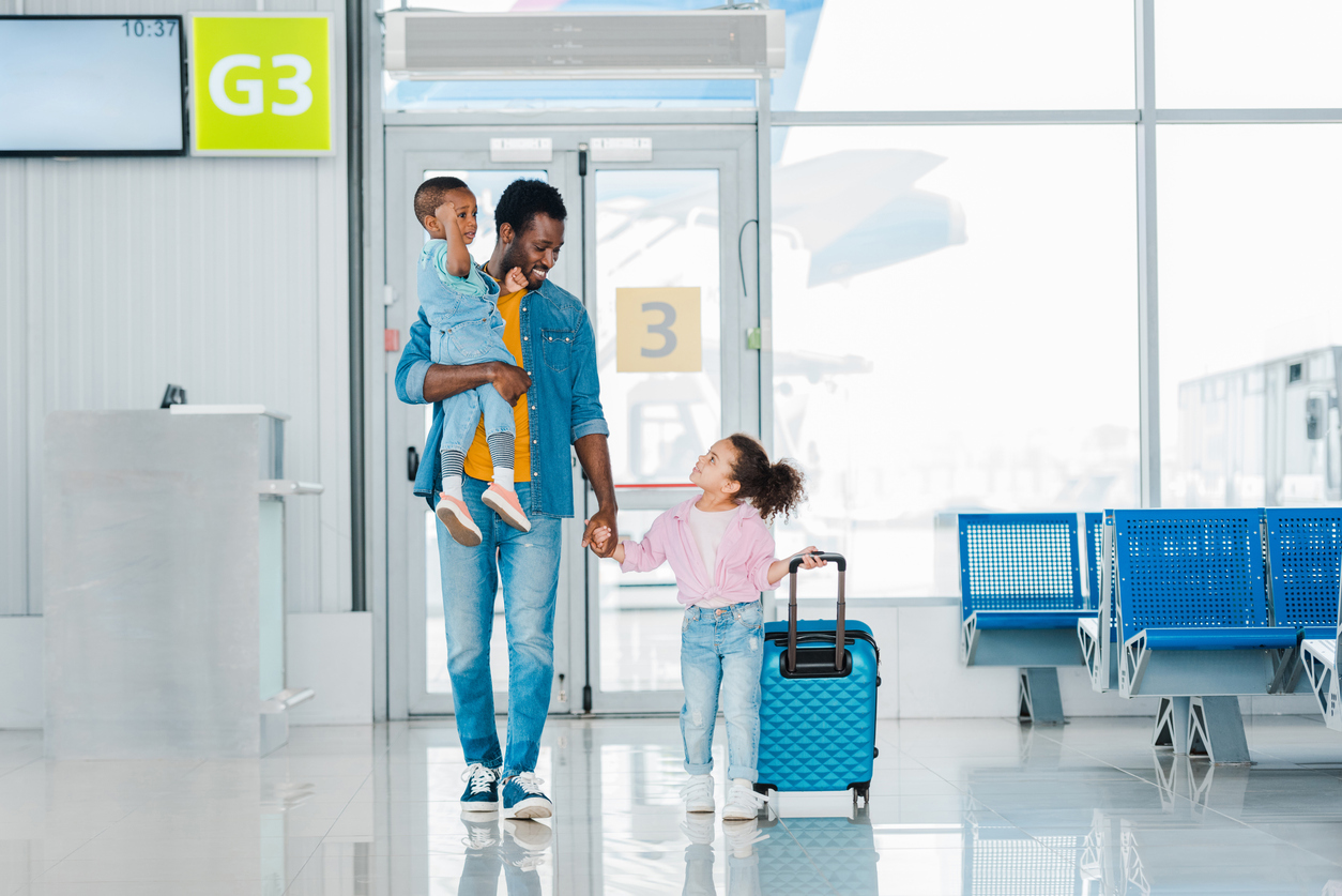Smiling Black father walking with children along waiting hall in airport.